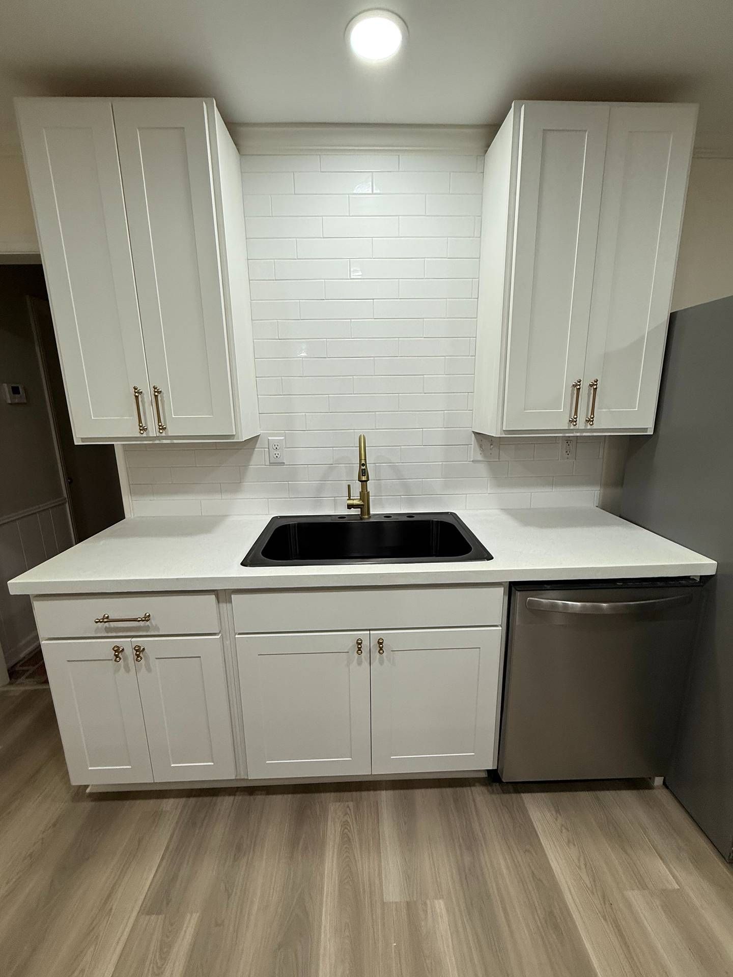 Small white kitchen with black sink, white cabinets, tile backsplash, and stainless dishwasher.