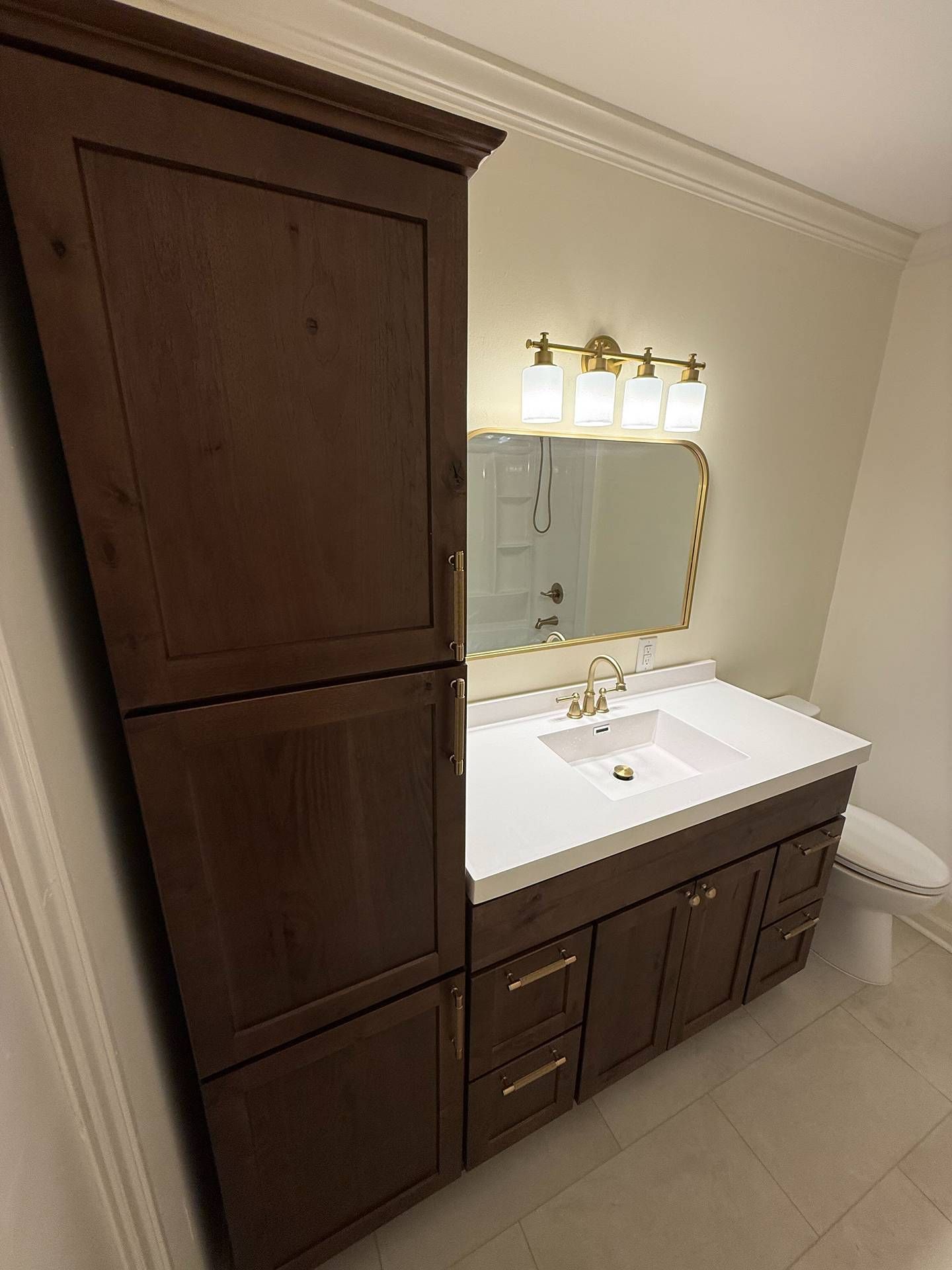 Bathroom vanity with dark wood cabinets, white sink, and mirrored light fixture beside a tall storage cabinet