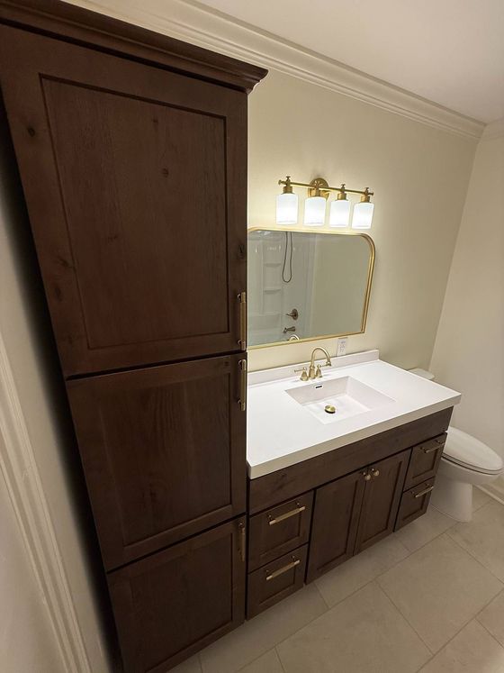Bathroom vanity with dark wood cabinets, white sink, and mirrored light fixture beside a tall storage cabinet