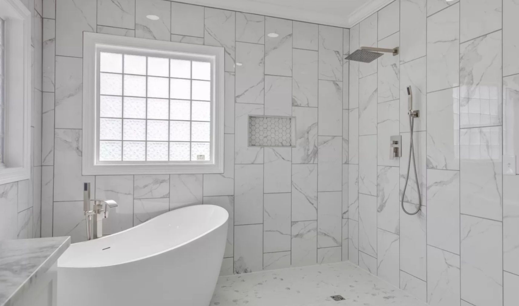 Modern white marble bathroom with a freestanding tub, walk-in shower, and frosted window