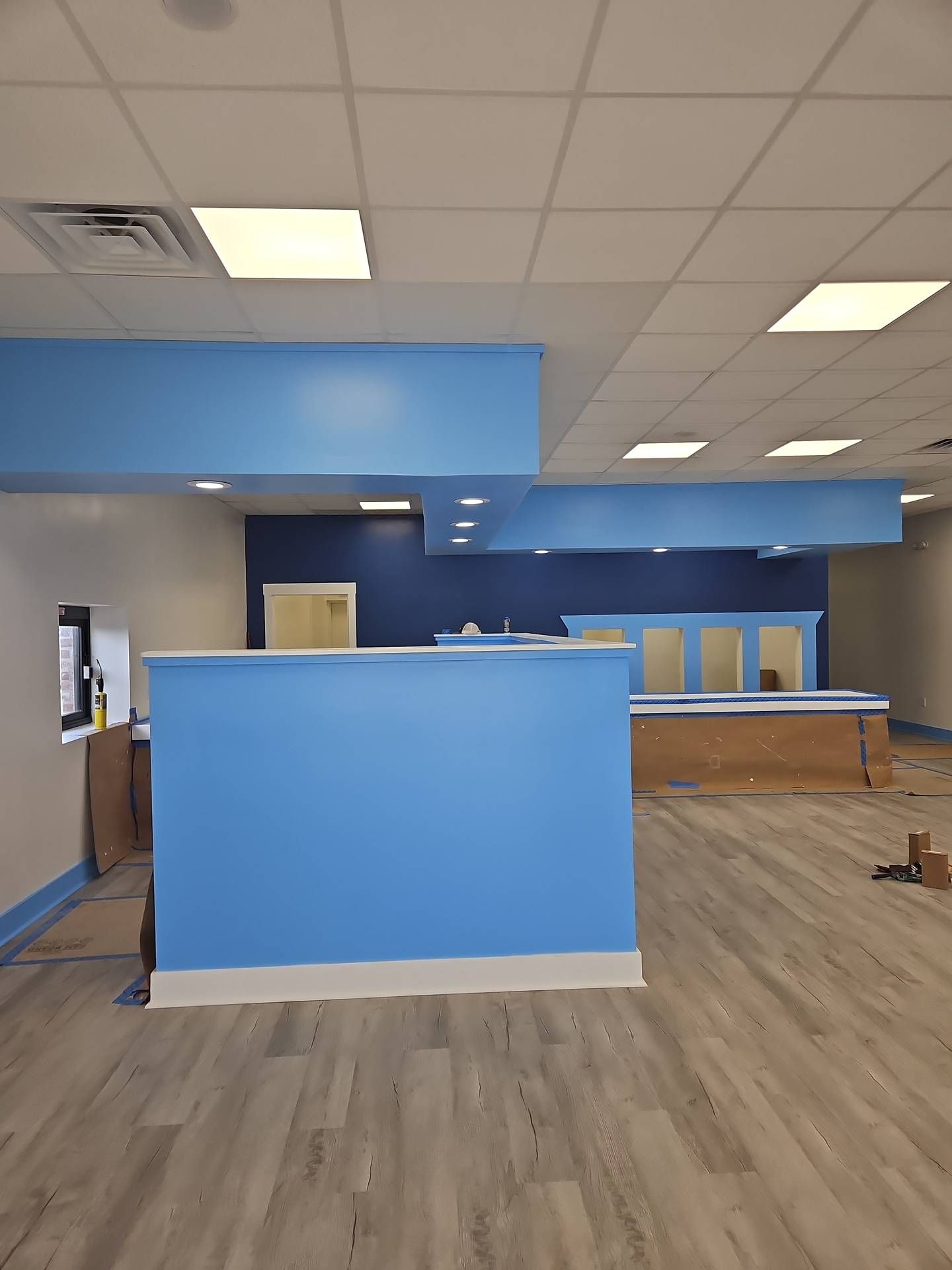 Empty office interior with blue walls, reception desk, wood-look flooring, and fluorescent ceiling lights