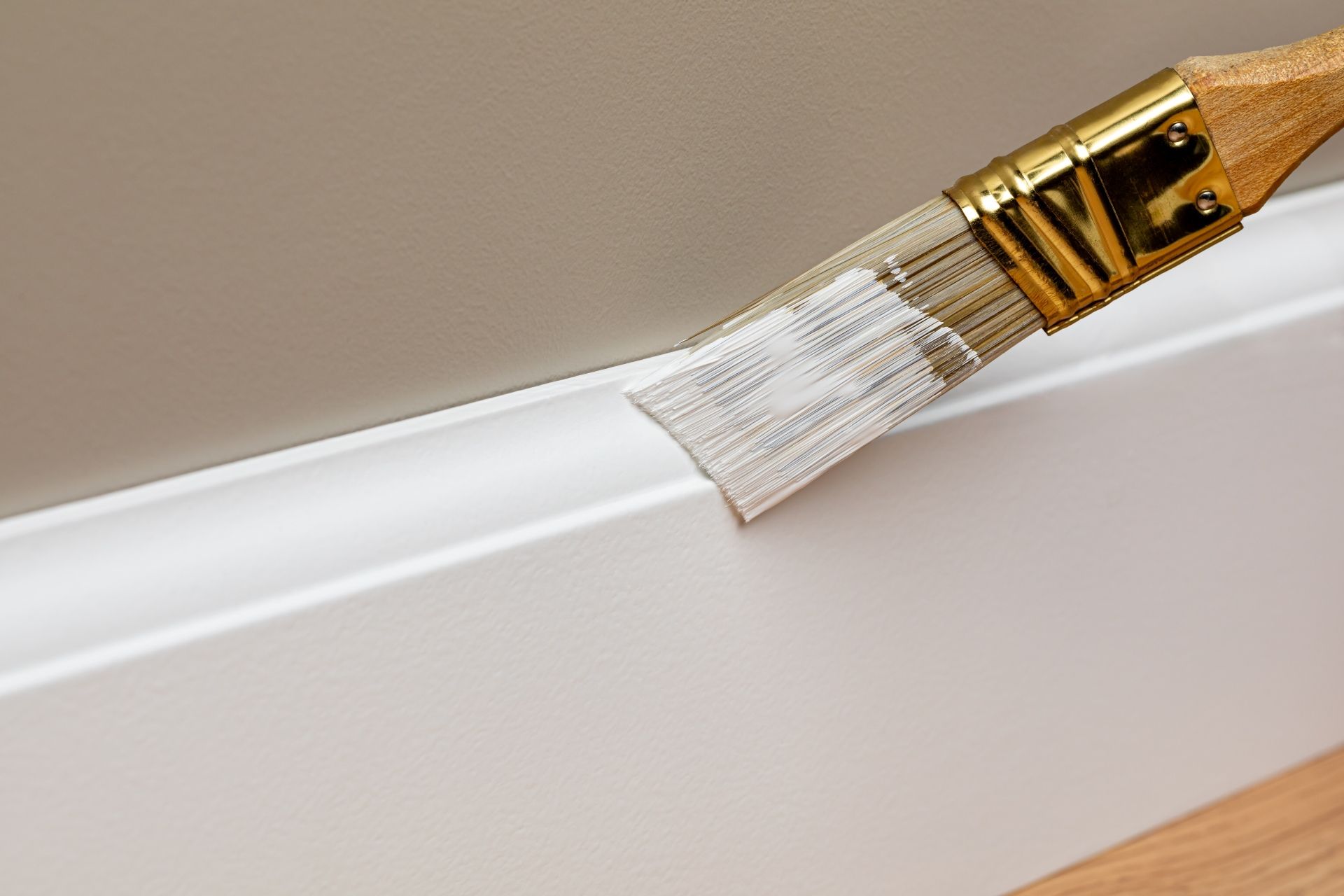 Paintbrush applying white paint to a curved wall edge