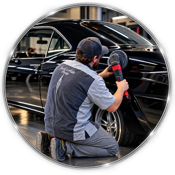 Detailer polishing a black classic car with a buffer in a garage