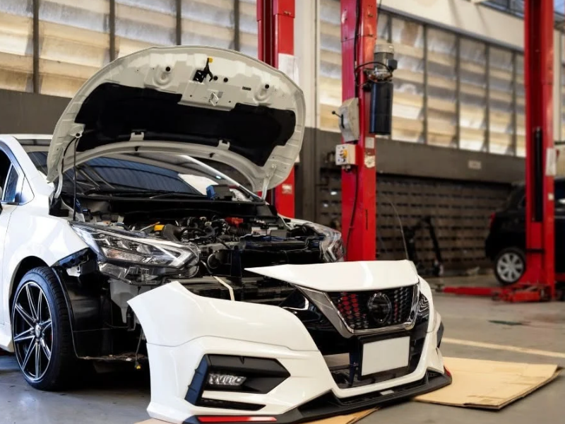 Mechanic leaning over a car engine with the hood open in a repair shop