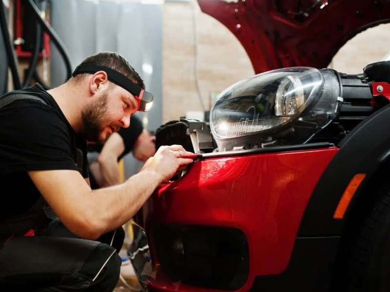 Man smiling beside a glossy black car, reflected in the paint inside an auto workshop