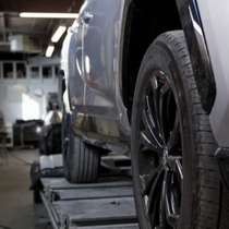 Two people in a garage beside a covered sports car, with sunlight through large windows.