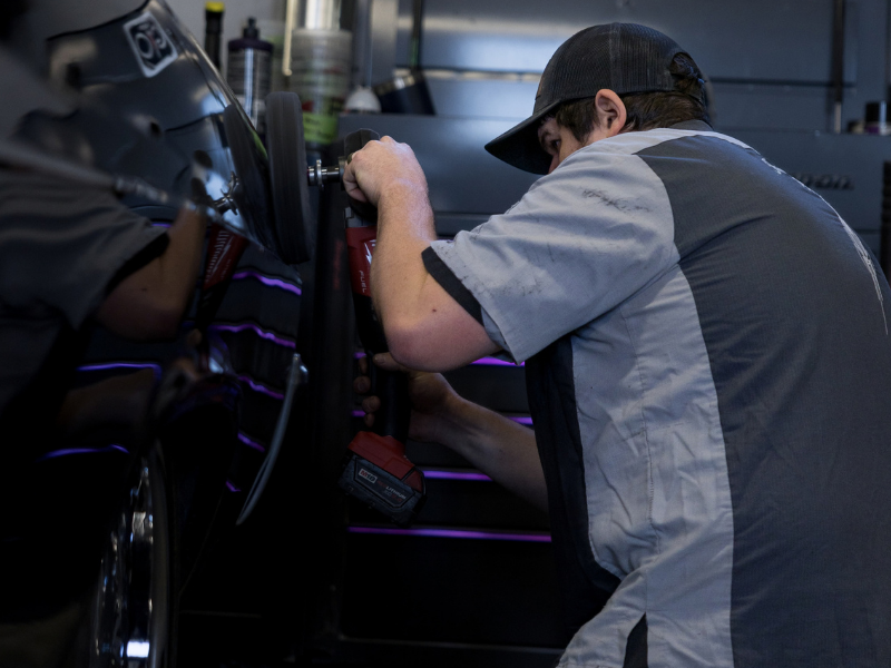Hands polishing a black car hood with a yellow buffer pad