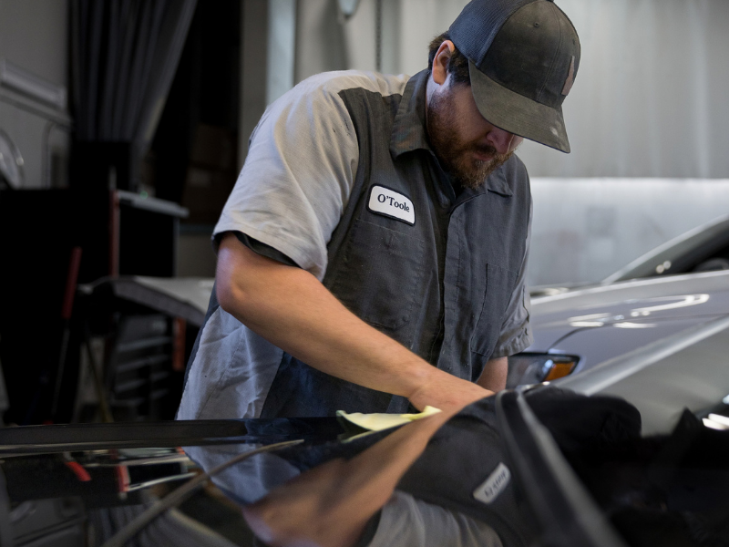 Hand polishing a car headlight beside a blue-covered hood