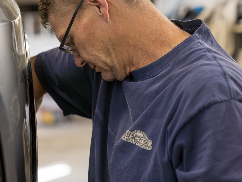 Mechanic cutting a car&rsquo;s exhaust with a grinder, sending bright sparks across a wet street.