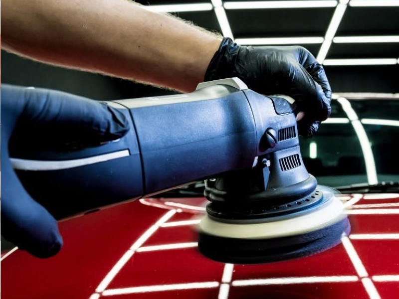 Spray gun coating a glossy black car part in a workshop booth