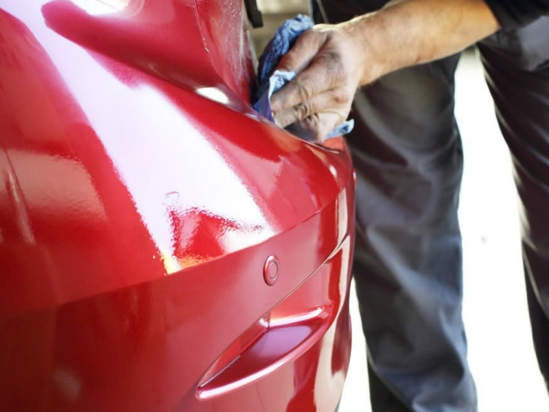 Hands polishing a black car hood with a buffer machine, reflecting the surface