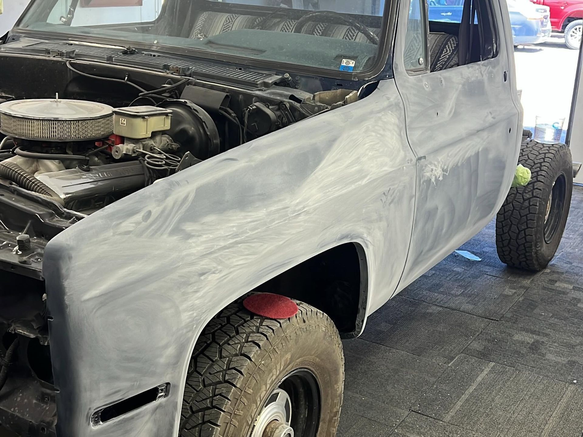 White pickup truck with primer-coated body panels and exposed front engine in a garage.