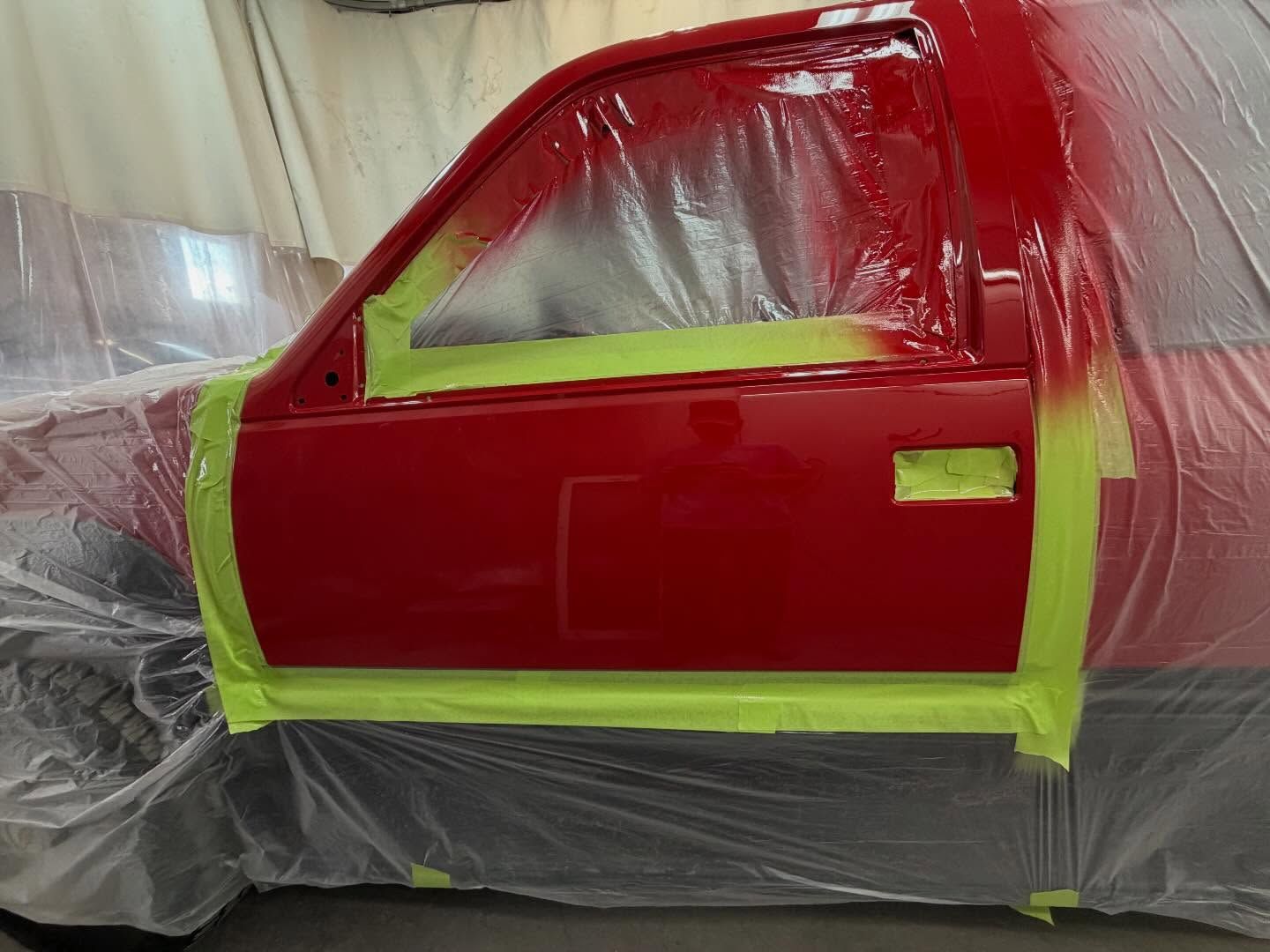 Red car door masked with tape and plastic during paint prep in a body shop