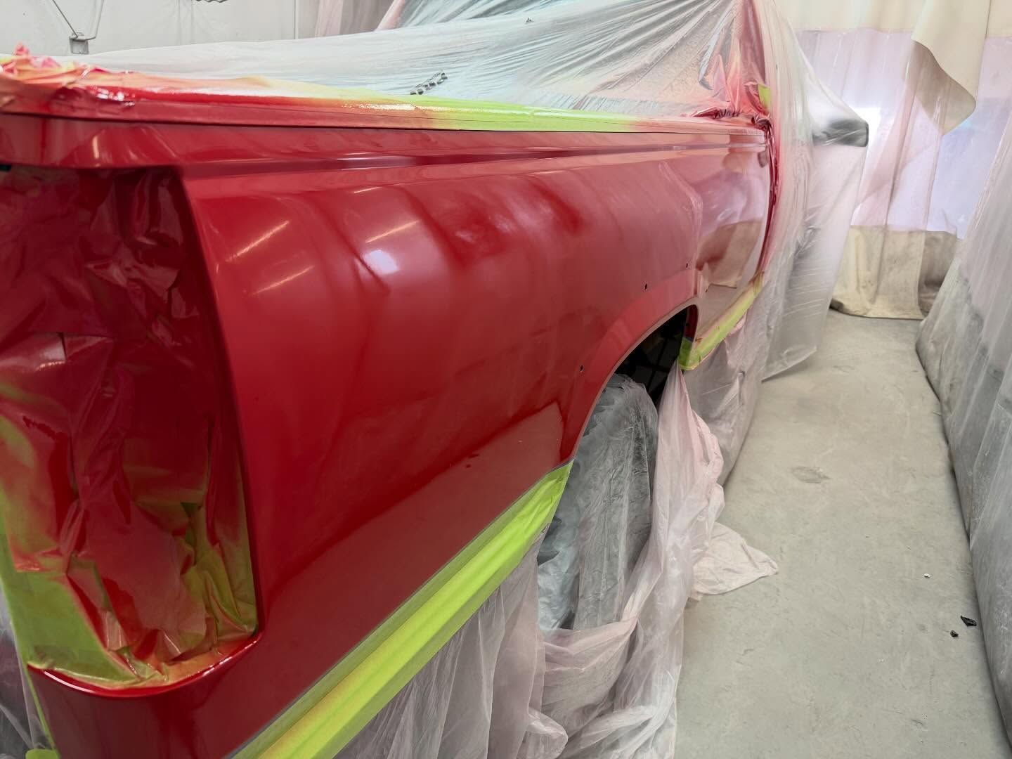 Red car panel masked for painting with tape and plastic sheeting in a workshop