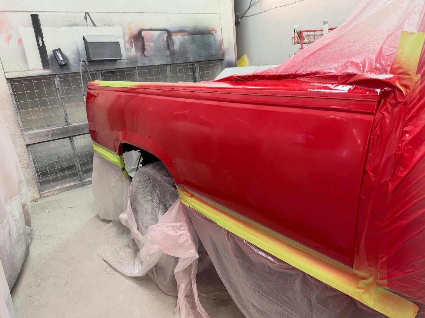 Red car body in a paint shop, masked with plastic and tape, being sprayed glossy red