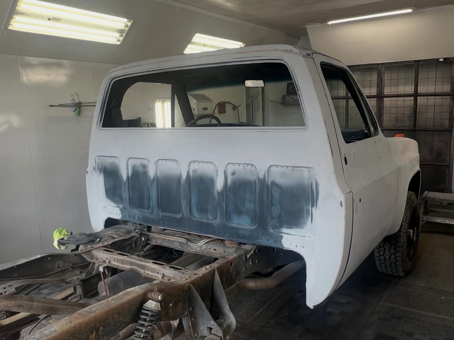 Primer-coated pickup truck body in a garage, with the rear bed removed and the chassis exposed.