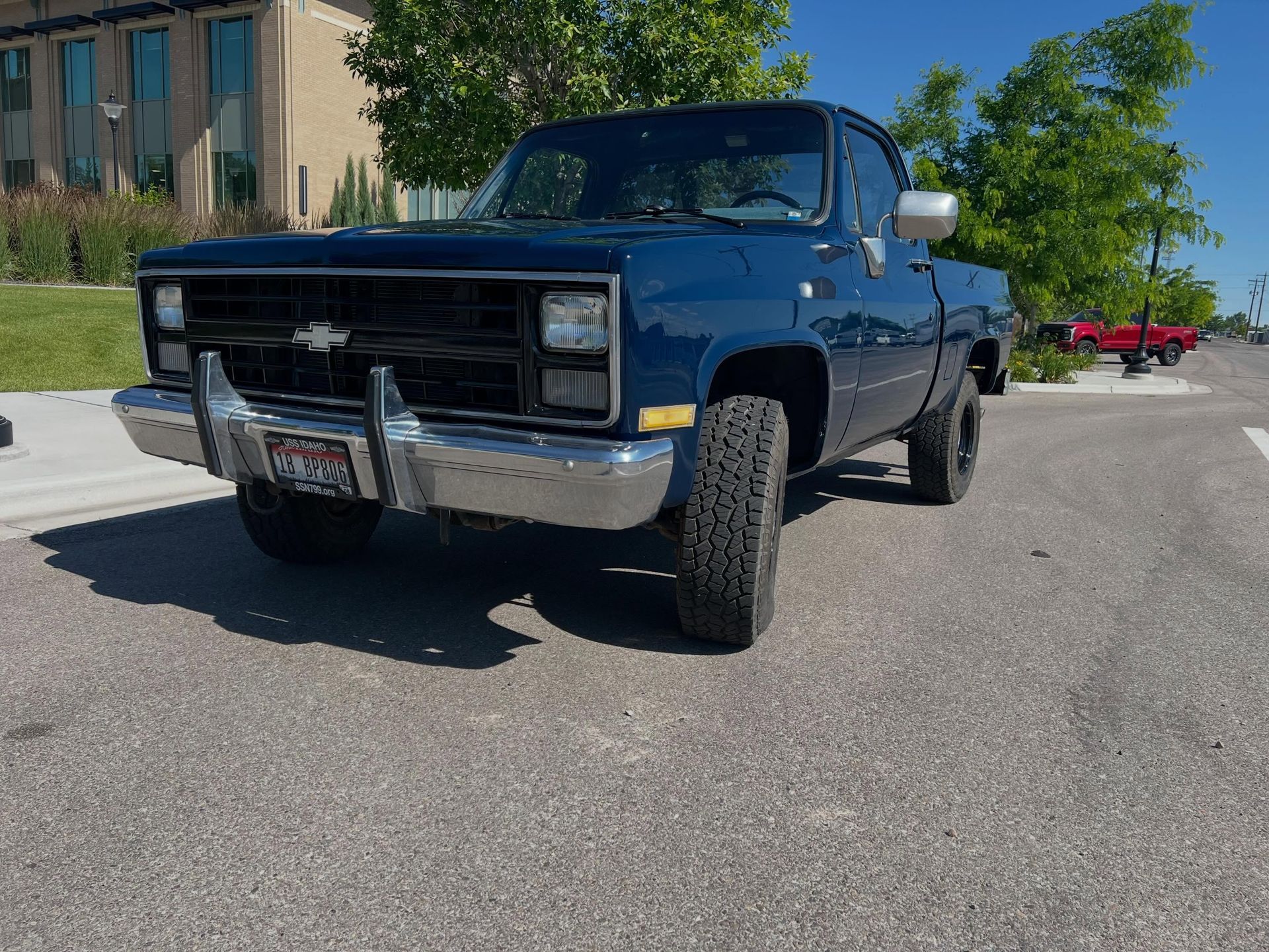 Blue pickup truck parked on a sunny street near a building and trees