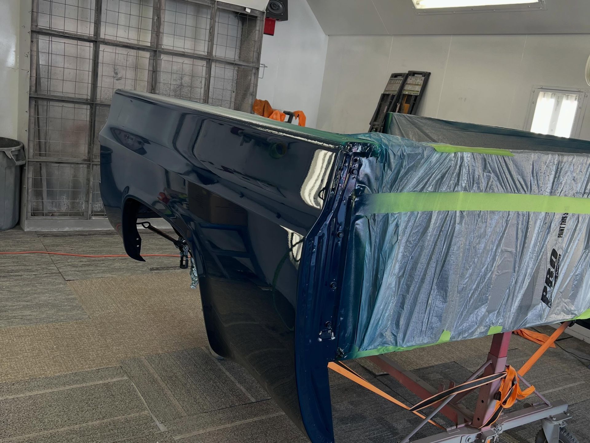 Blue car body panel masked with tape and plastic in a body shop, awaiting paint