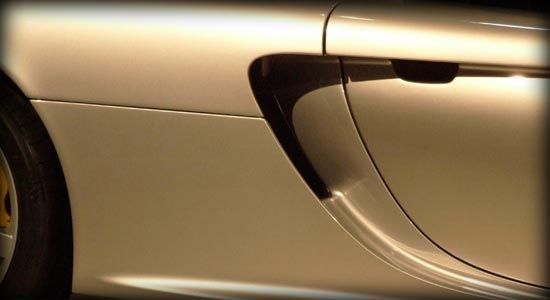 Close-up of a silver sports car door and side panel with a sculpted air intake.