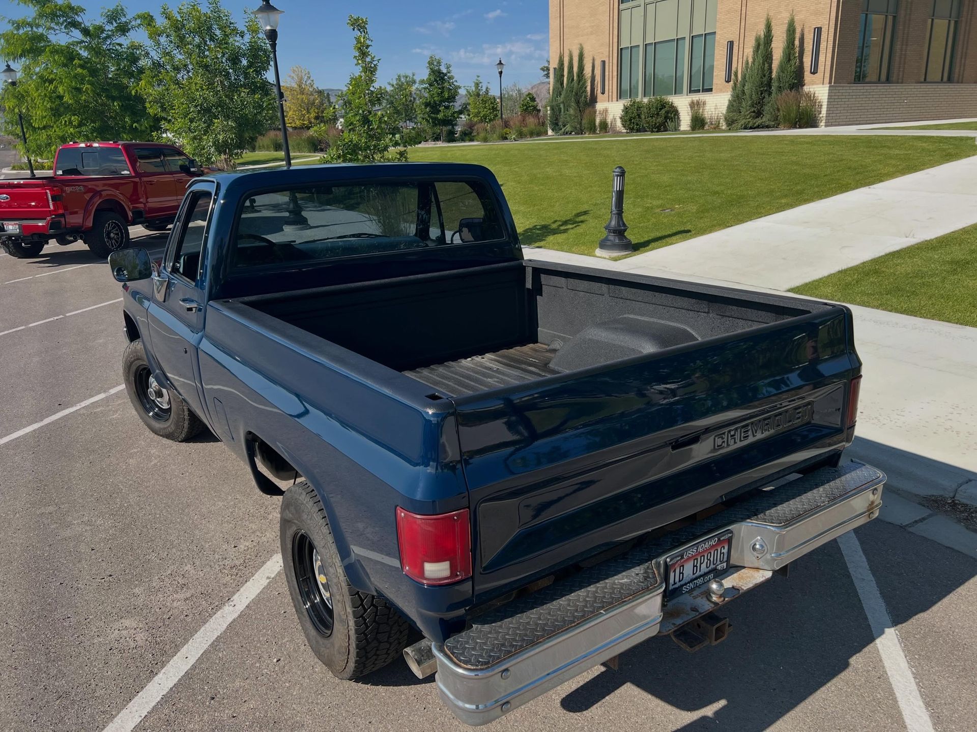 Blue pickup truck parked on a sunny campus street, rear three-quarter view.