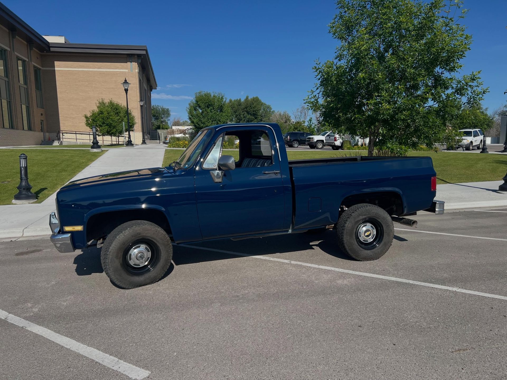 Blue pickup truck parked in a lot beside a brick building under a clear sky.