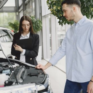 Two people inspecting a car engine in a bright dealership showroom