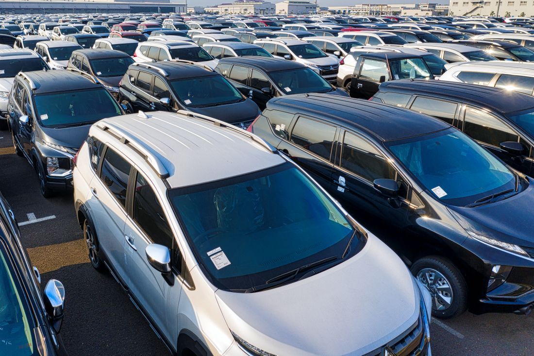 Rows of parked cars in a crowded outdoor lot, mostly white and dark-colored vehicles.