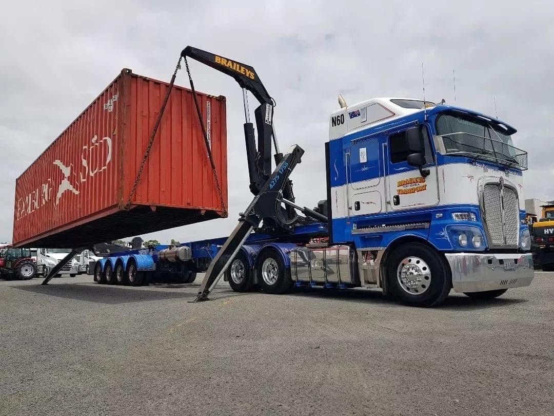 A blue and white semi truck is carrying a red shipping container.