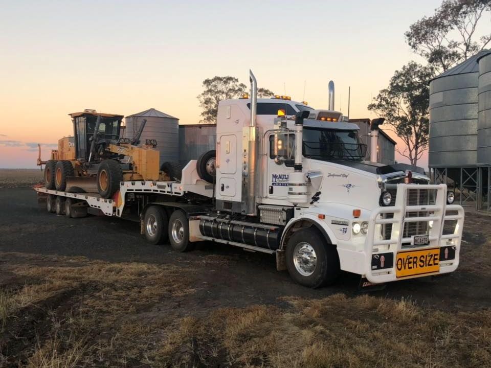 Prime mover and drop deck trailer towing a Caterpillar grader