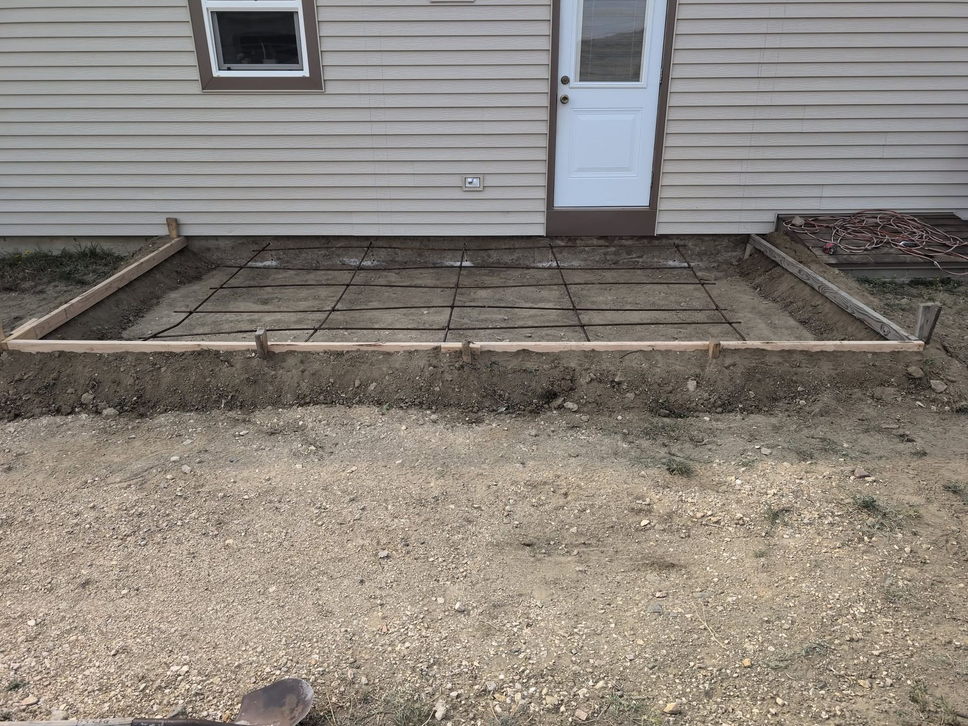 Patio under construction beside a house, with wooden framing and paver stones around a back door