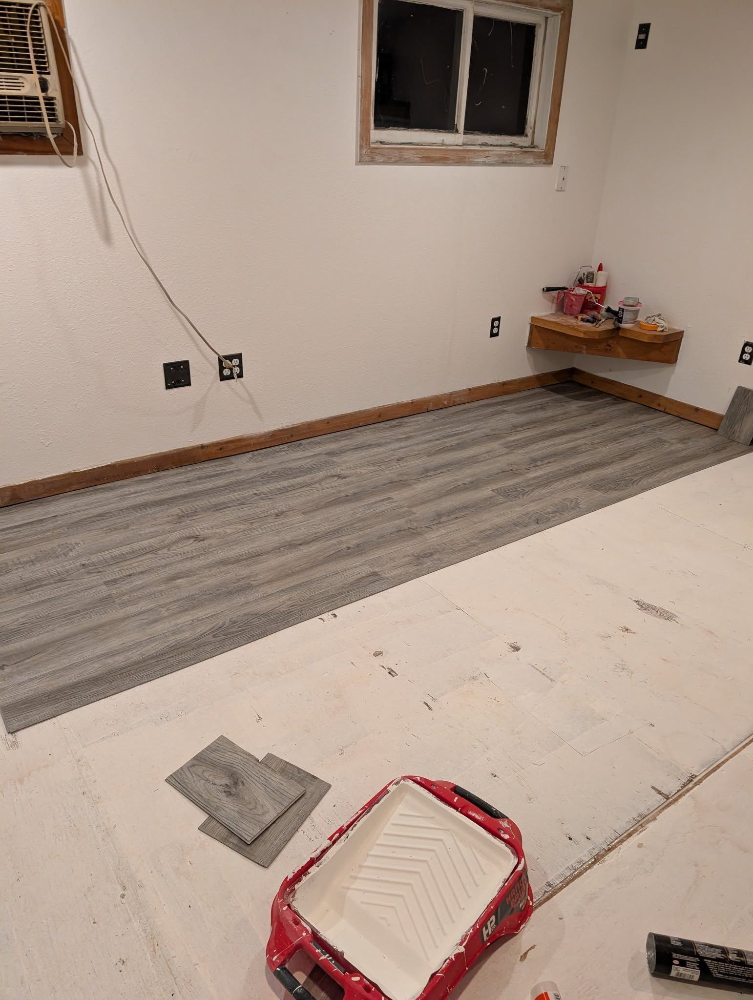 Unfinished room with gray flooring, exposed wall outlets, a window, and painting supplies on the floor.