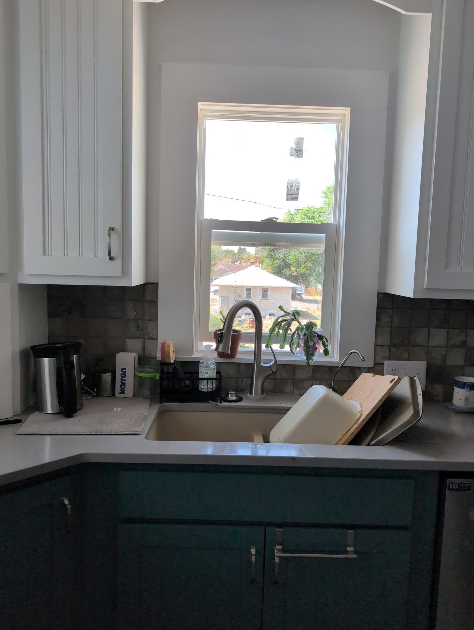 Kitchen sink beneath a window, with white cabinets and a dish rack on the counter