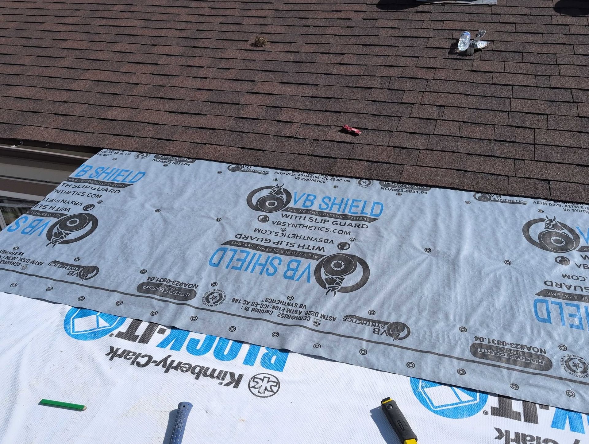 Roof with partially installed underlayment and shingles, including blue-and-white protective roofing material.