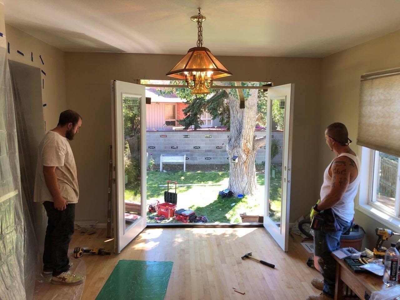 Two men working in a room with open doors, sunlight, tools, and supplies on the floor