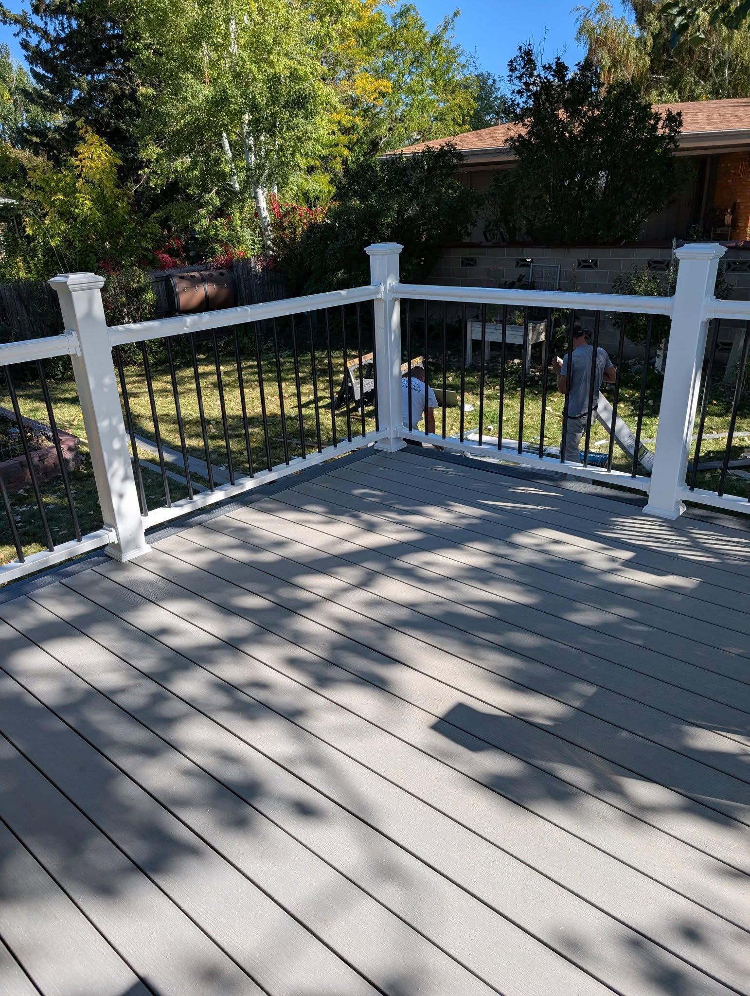 White deck with railing overlooking a green yard and trees in sunlight