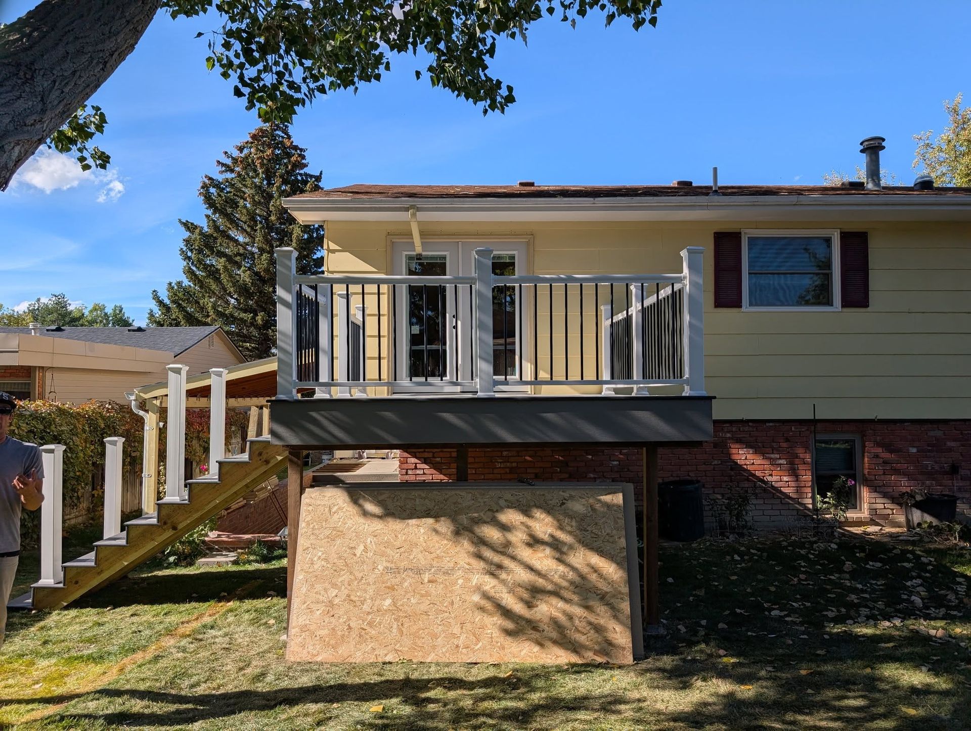 Back deck with white railing and stairs beside a beige house on a sunny day