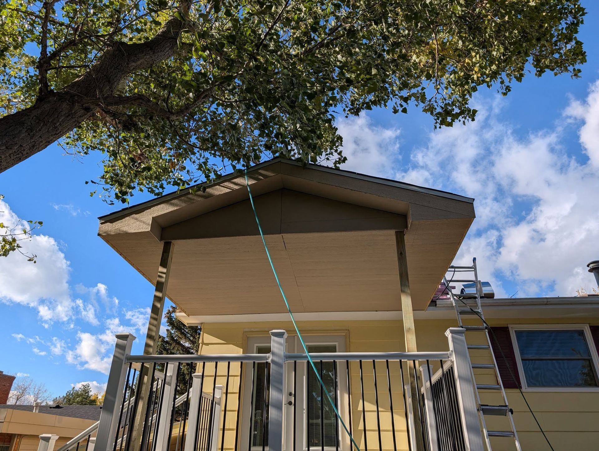 Backyard patio with a raised deck, metal railing, and awning under a tree on a sunny day