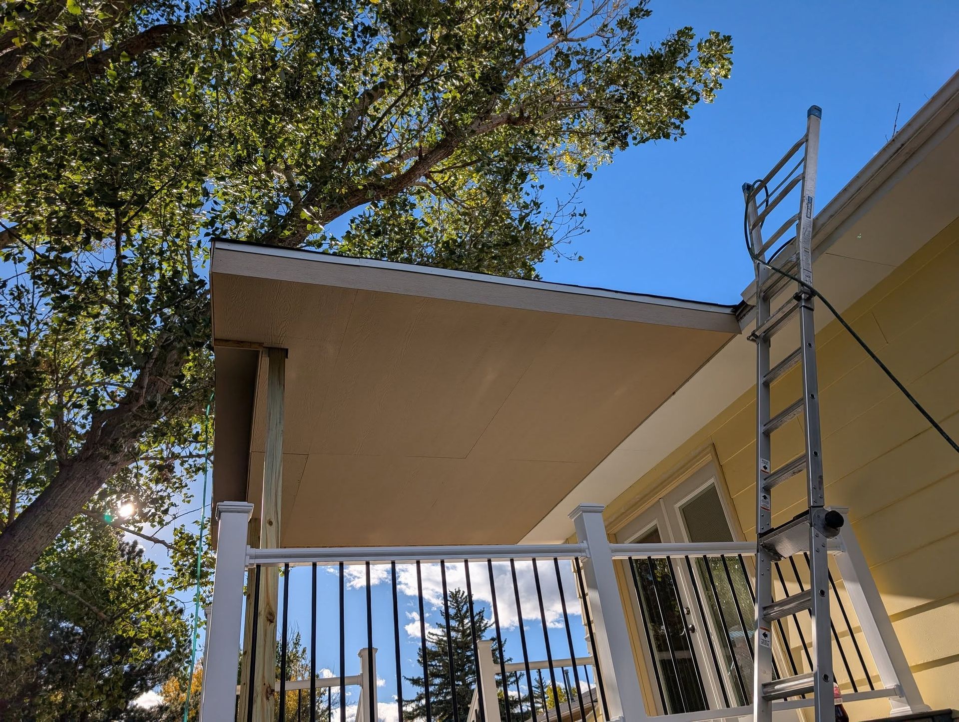Balcony with white railings under a beige roof, framed by trees and blue sky