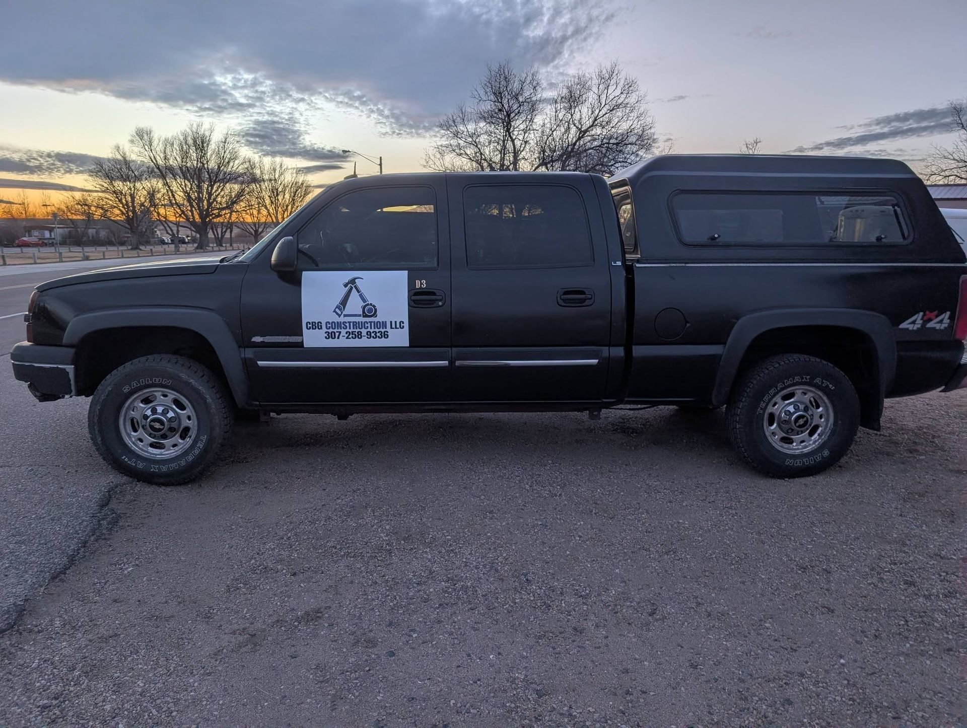 Black pickup truck with company logo parked on gravel at sunset.