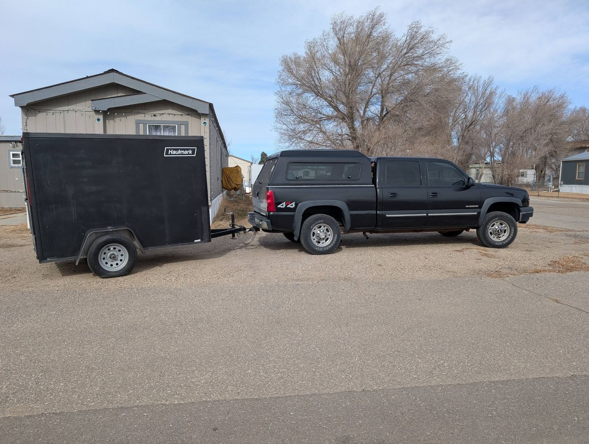 Black pickup truck towing a black enclosed trailer on a suburban street under a clear sky