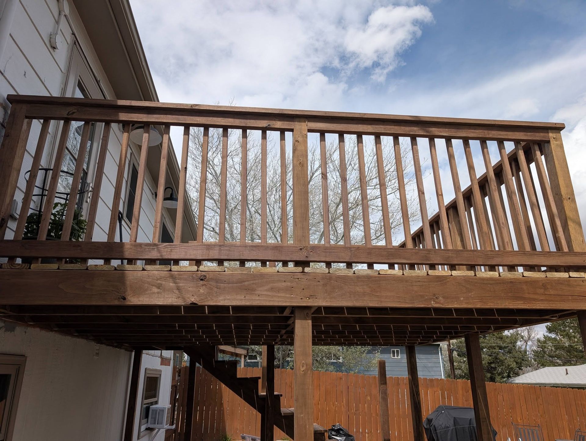 Wooden deck and railing attached to a house, viewed from below against a cloudy sky.
