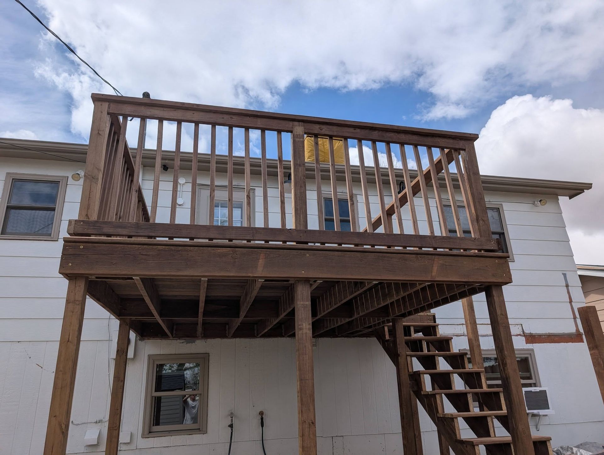 Partially built wooden deck attached to a white house, with stairs and exposed framing underneath.