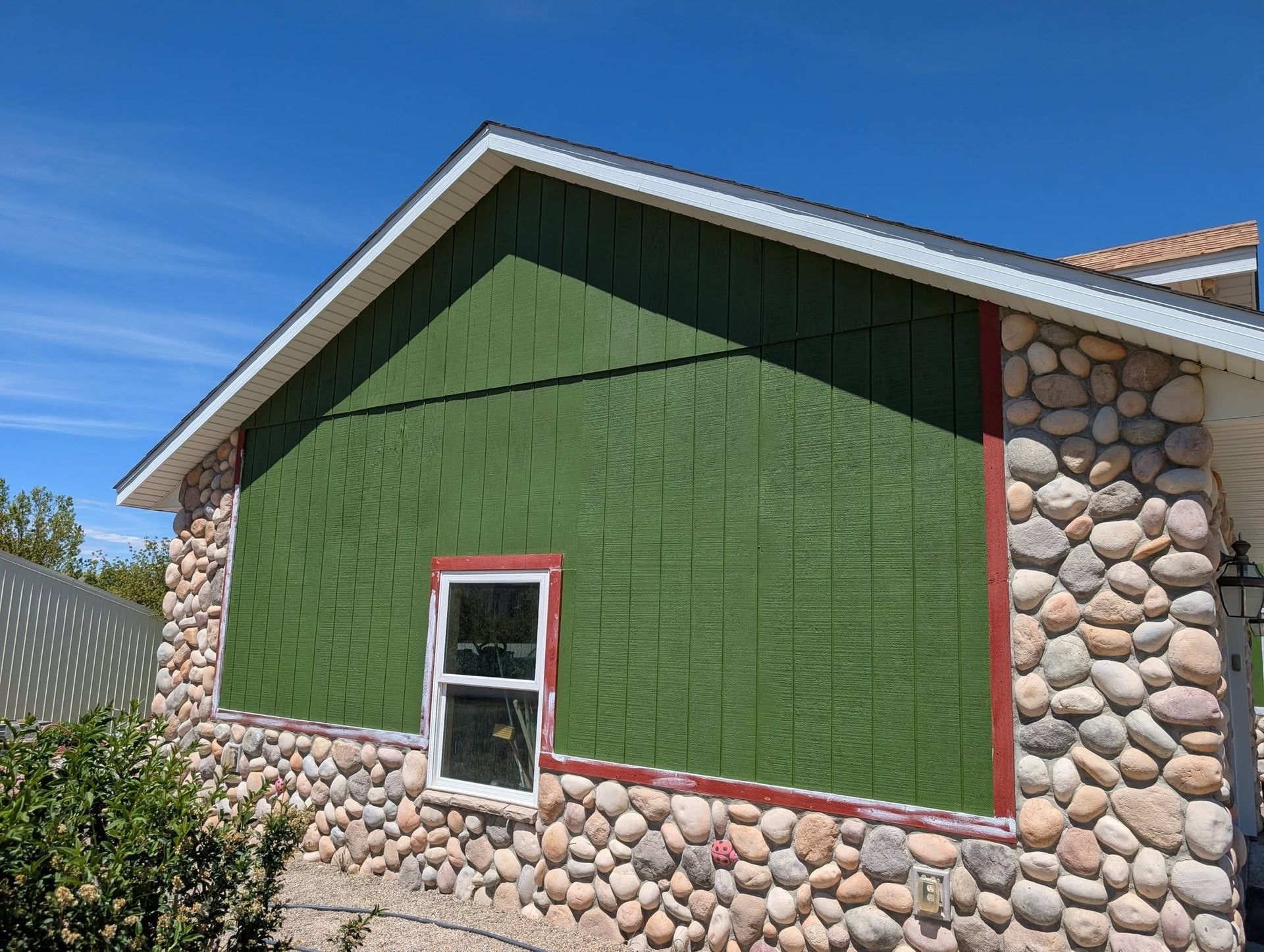 Green house exterior with stone accents and a small window under a blue sky