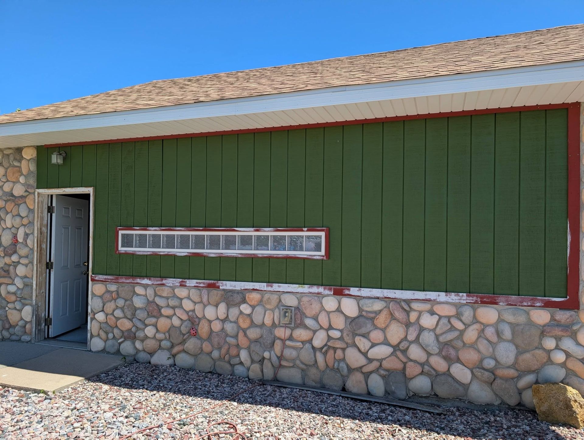 Green building with stone base, small window, and open door under a tiled roof.