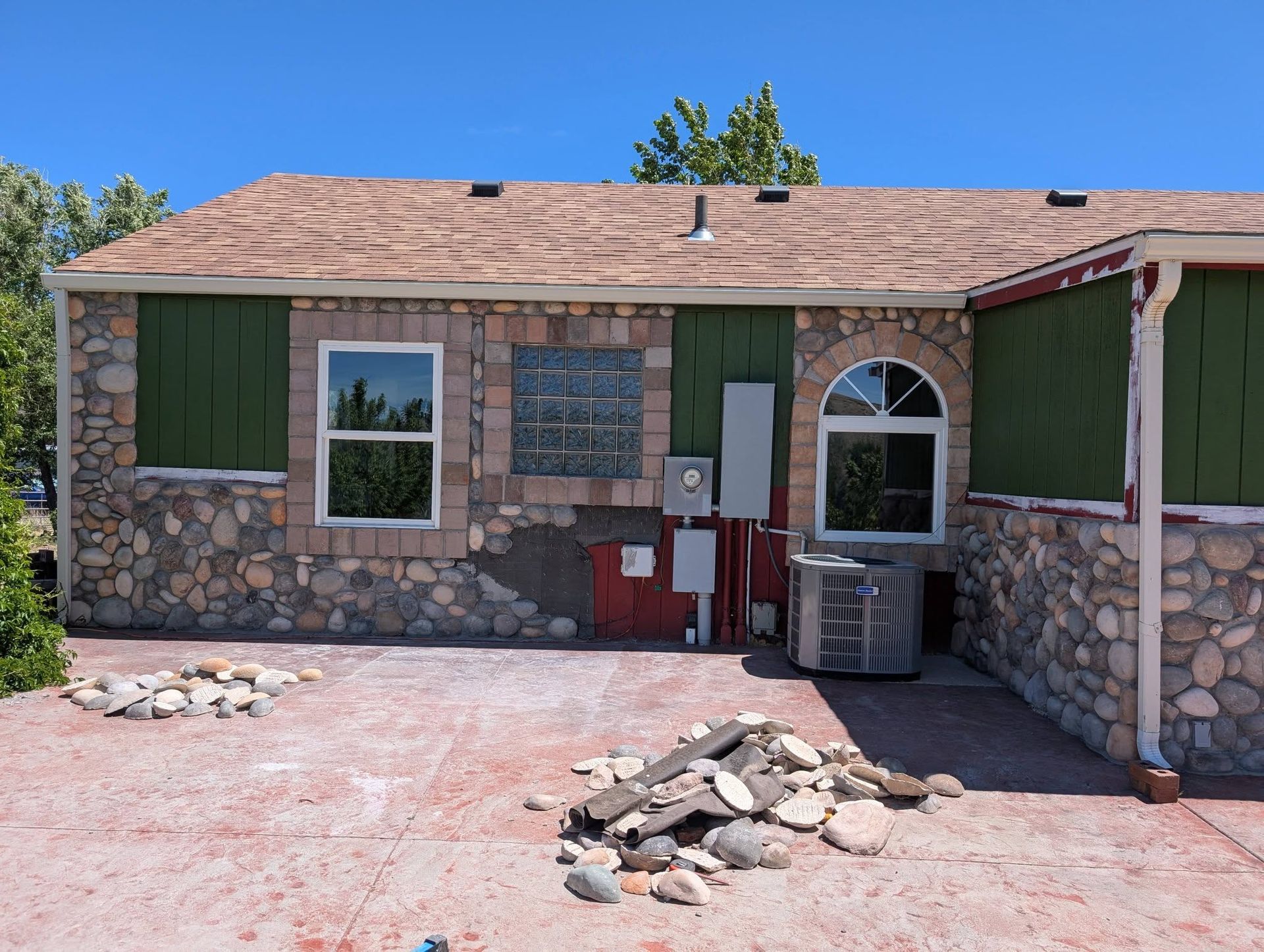Stone house exterior with green shutters, arched window, and rubble piles in a dusty yard