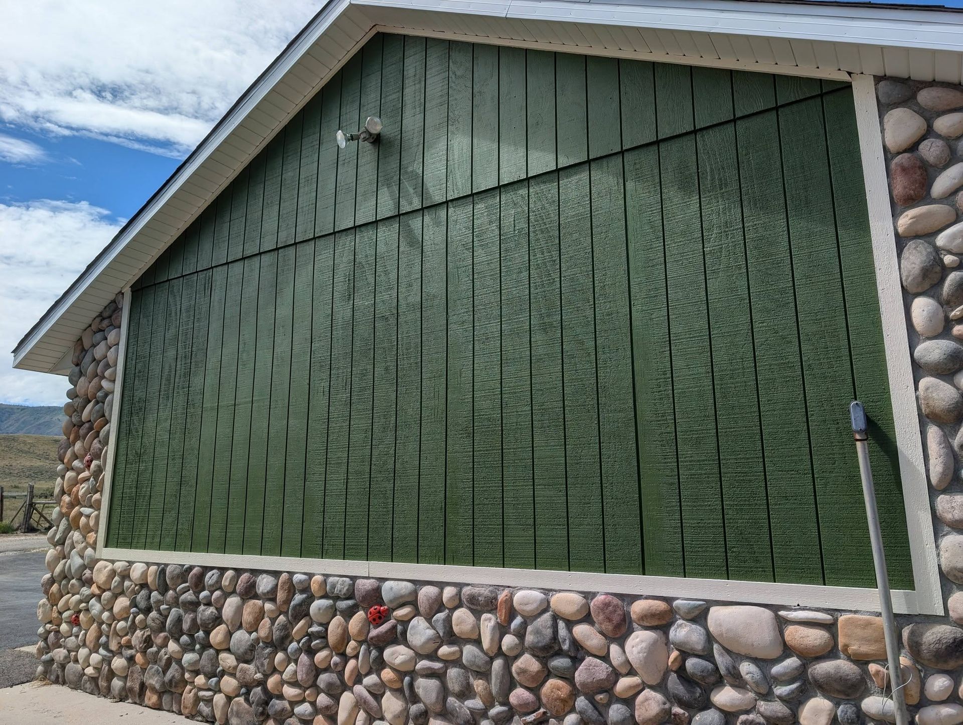 Green house wall with pebble stone base under a cloudy sky