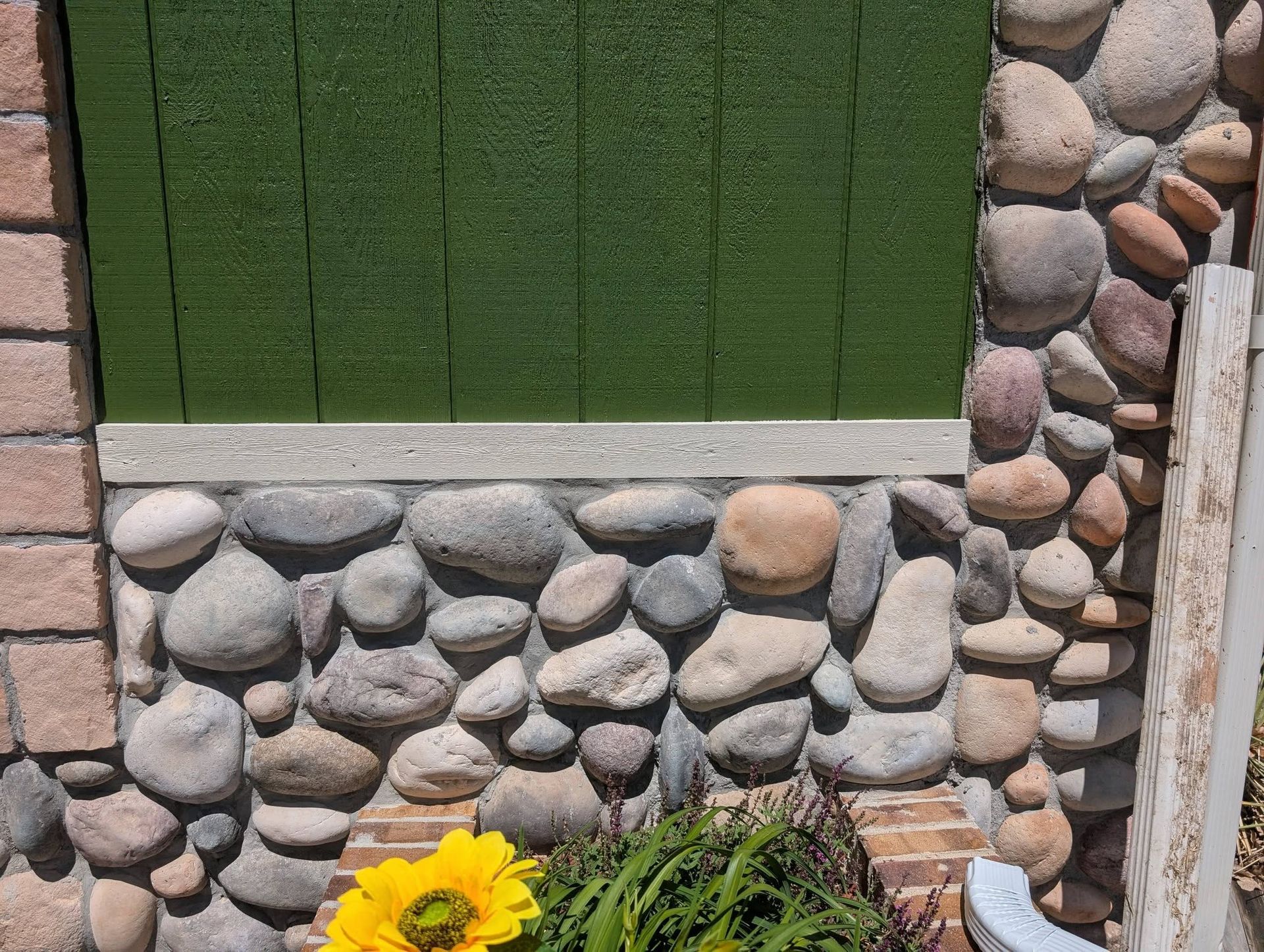 Green window box with white stones and a yellow flower below a window