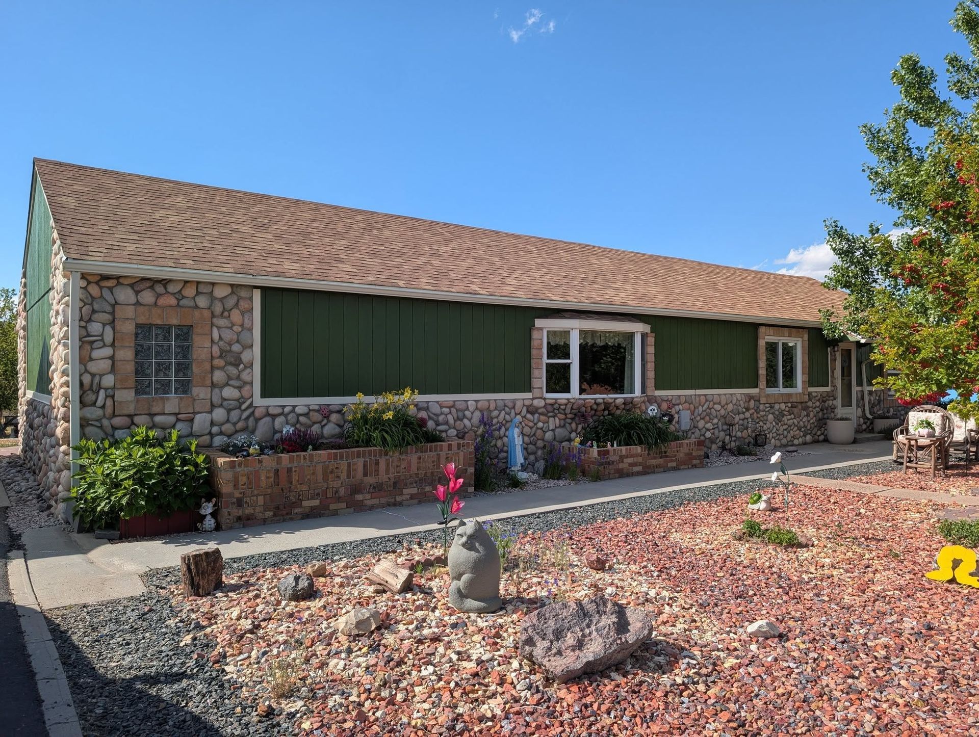Single-story stone house with tan roof, green shutters, and desert landscaping under a clear blue sky