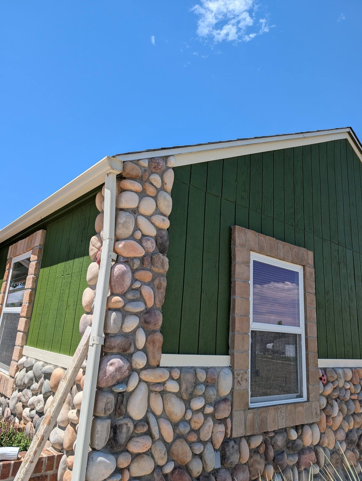 Stone-and-green-sided house exterior under a bright blue sky
