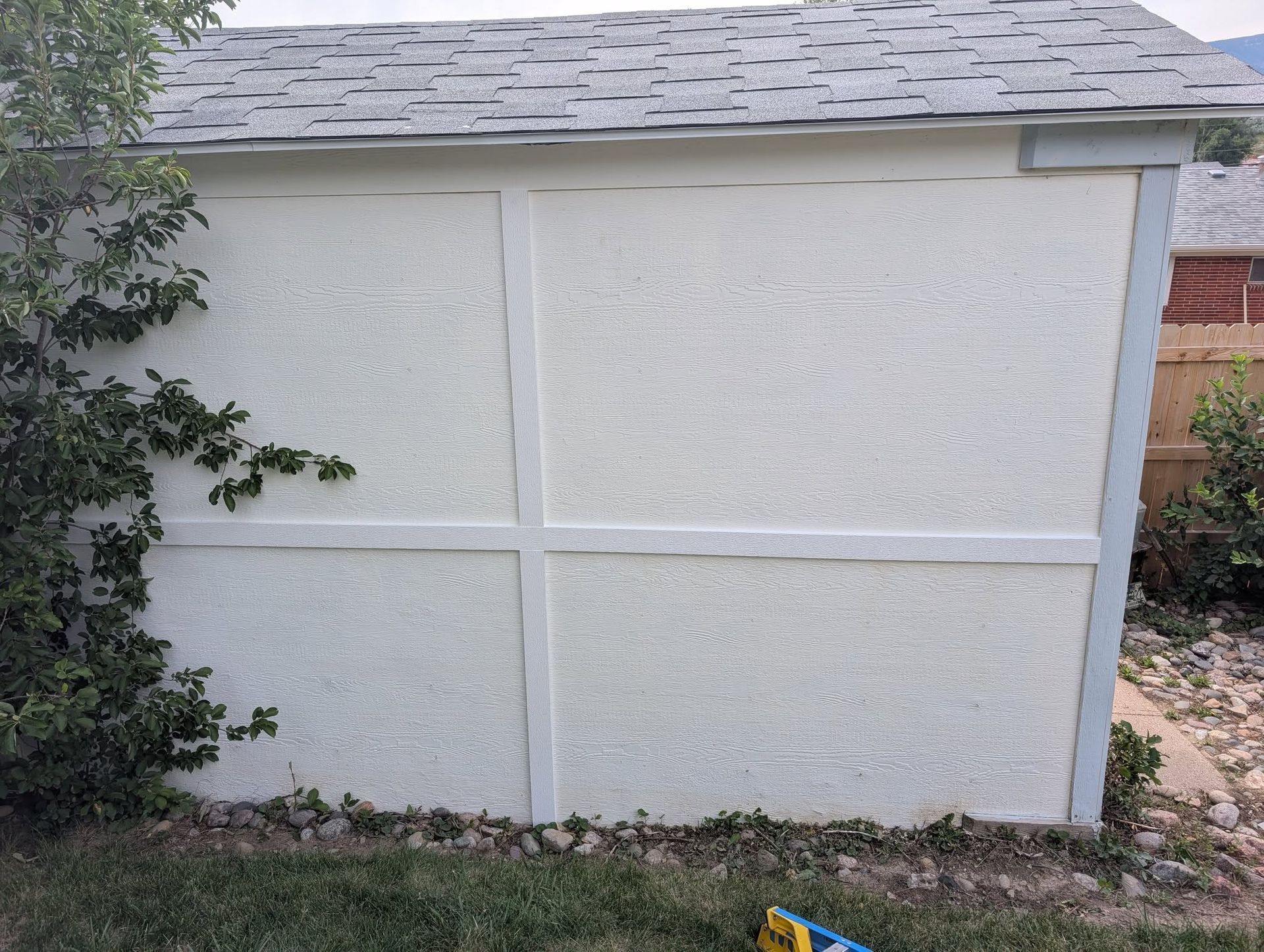 White stucco shed with a gray shingled roof and a small vine on the left side.